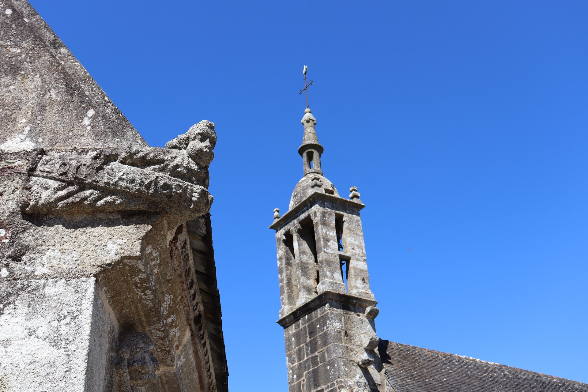 Sur fond de ciel bleu, vue sur le clocher et un détail de l'ossuaire de l'église Saint-Edern